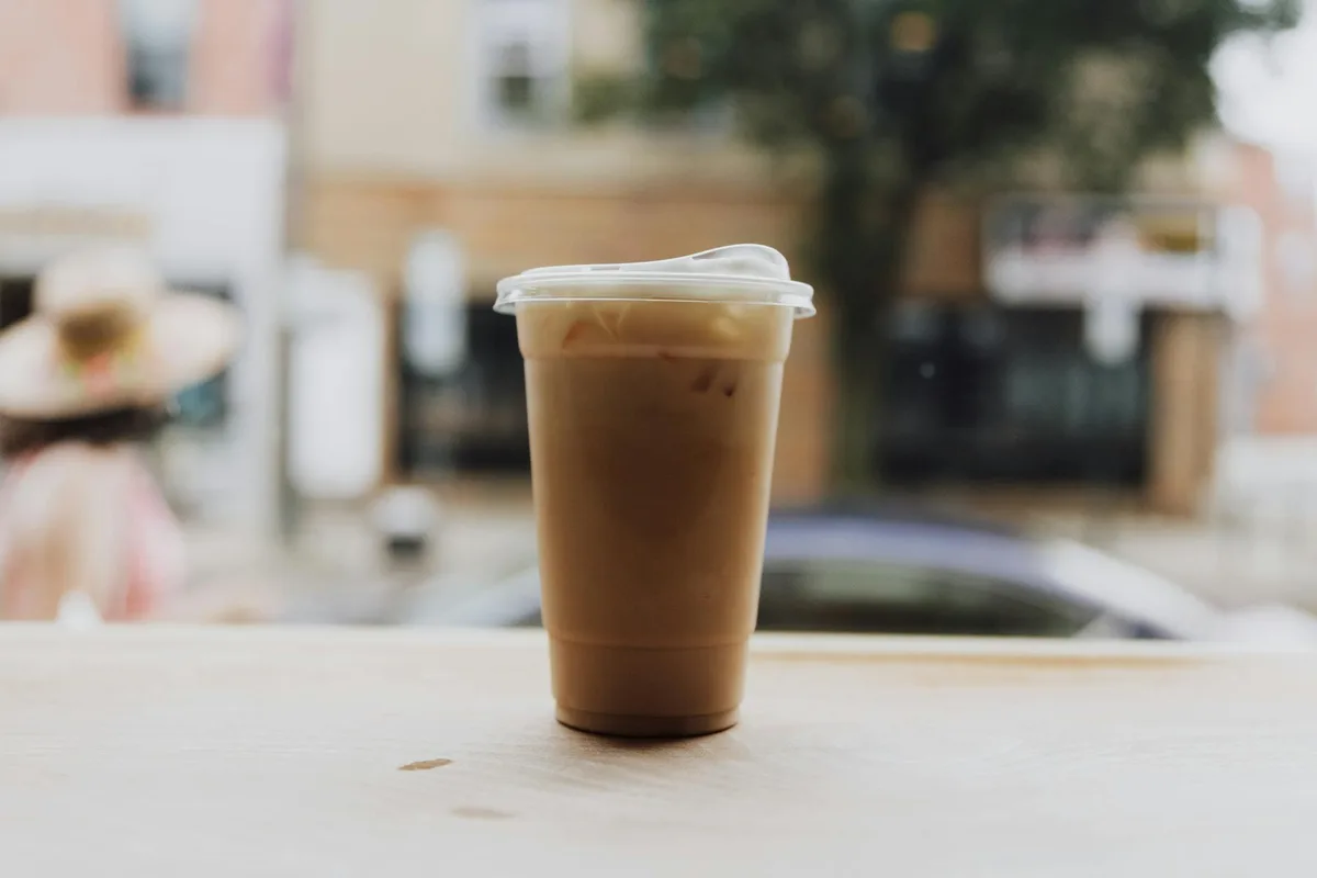 Iced coffee in a plastic cup on a table by a city street. Urban morning vibe.