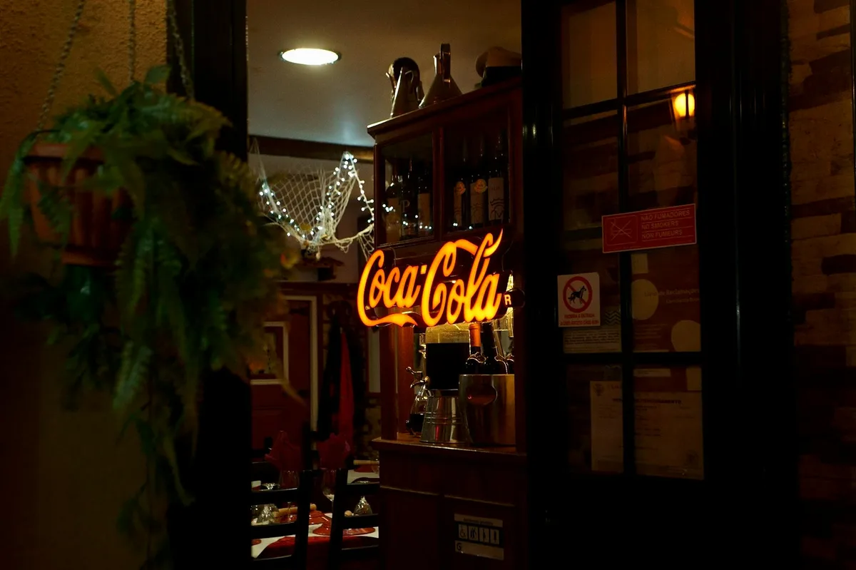 Cozy bar interior with neon Coca-Cola sign and warm ambiance lighting.
