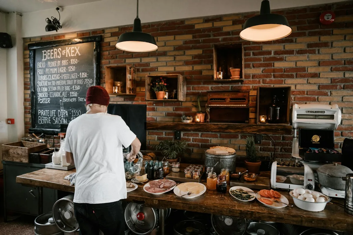 Person serving food in a cozy cafe with rustic brick walls and wooden buffet table.